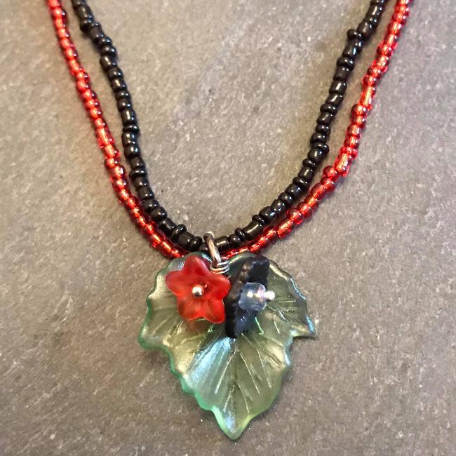 Necklace made from red and black seed beads with a flower and leaf pendant.